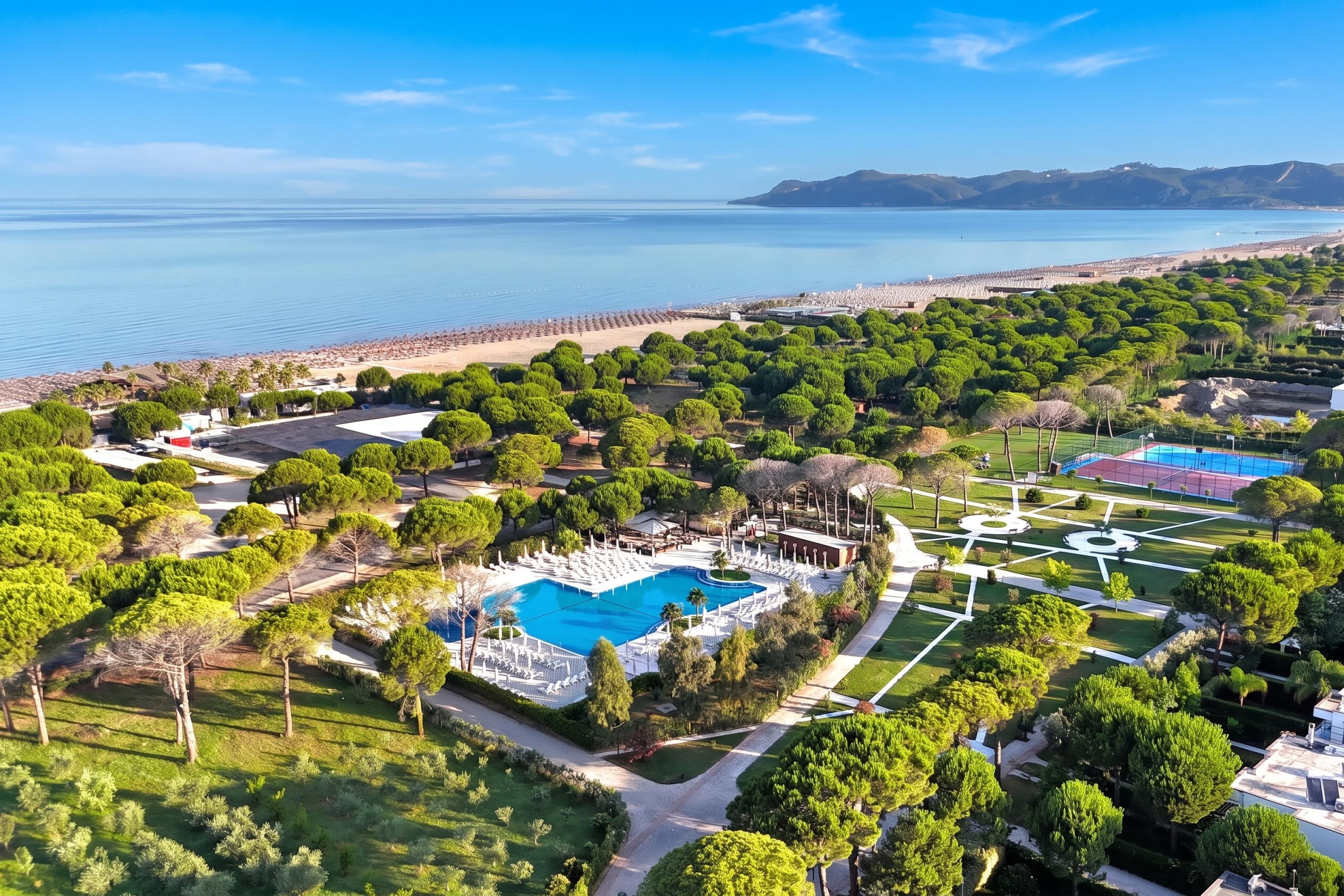 Eine Luftaufnahme eines Resorts mit Schwimmbad, angelegten Gärten und einem Strand.