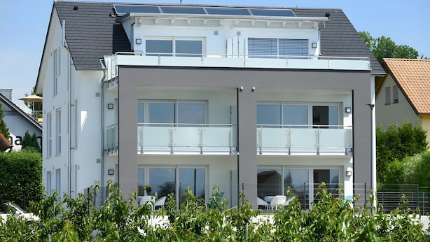 A modern two-story building with a balcony, large windows, and solar panels on the roof.