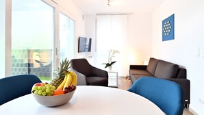 A modern living room with a round table, two armchairs, a sofa, a TV, and a large window.