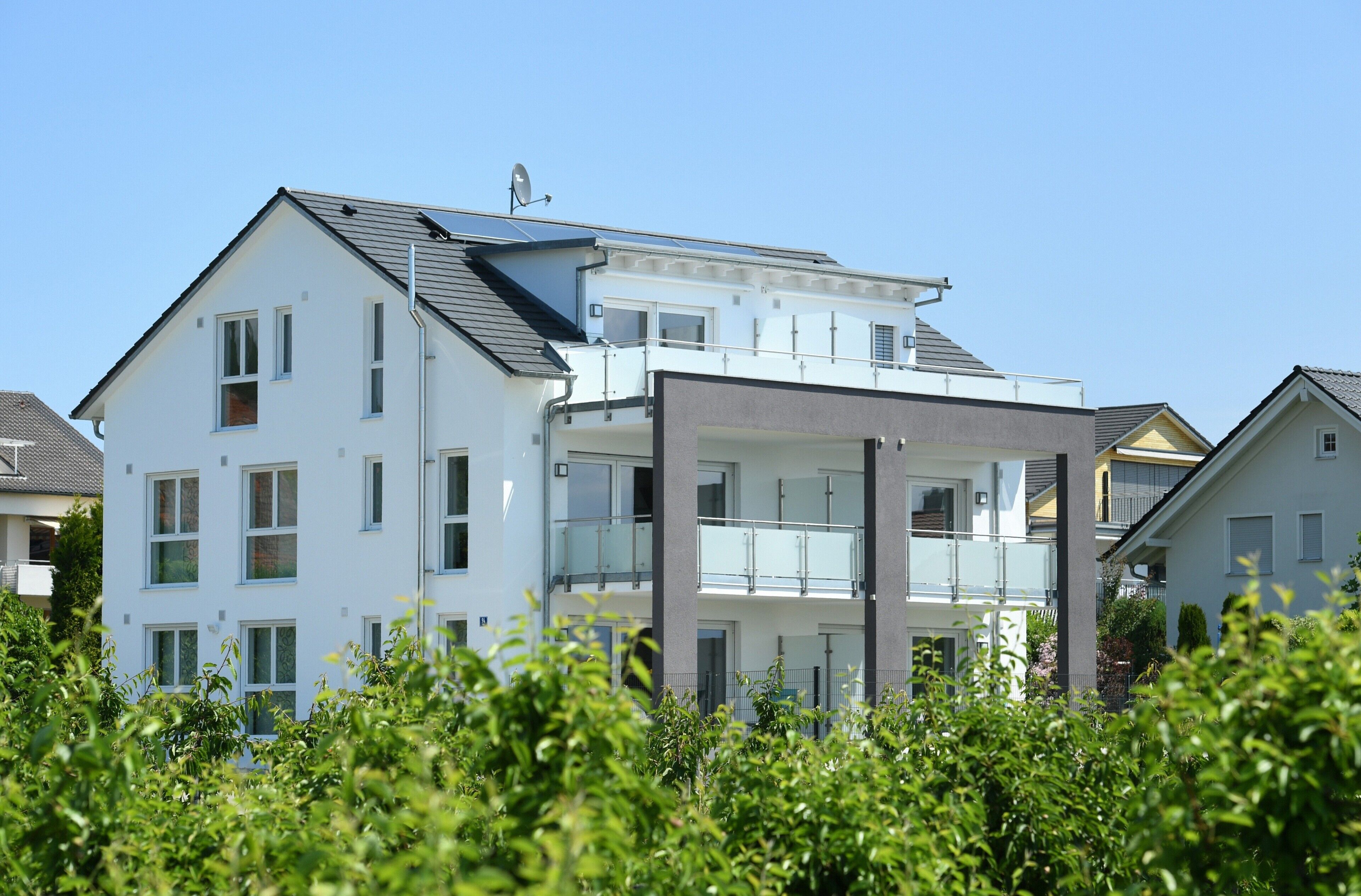 Un immeuble résidentiel moderne à plusieurs étages, doté de balcons, d’une antenne parabolique et de panneaux solaires.