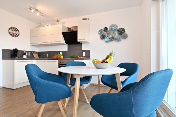 A modern kitchen with white cabinets, a black range hood, and a dining area with blue chairs and a white table.