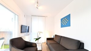 A modern living room with a sofa, armchair, TV, and a decorative wall piece.
