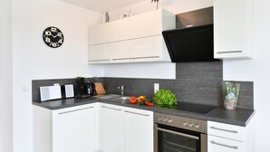 A modern kitchen with white cabinets, a black clock, a stove, and a sink.