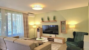 Ein Wohnzimmer mit einer Couch, einem Fernseher, einem Couchtisch und einem Sessel.
