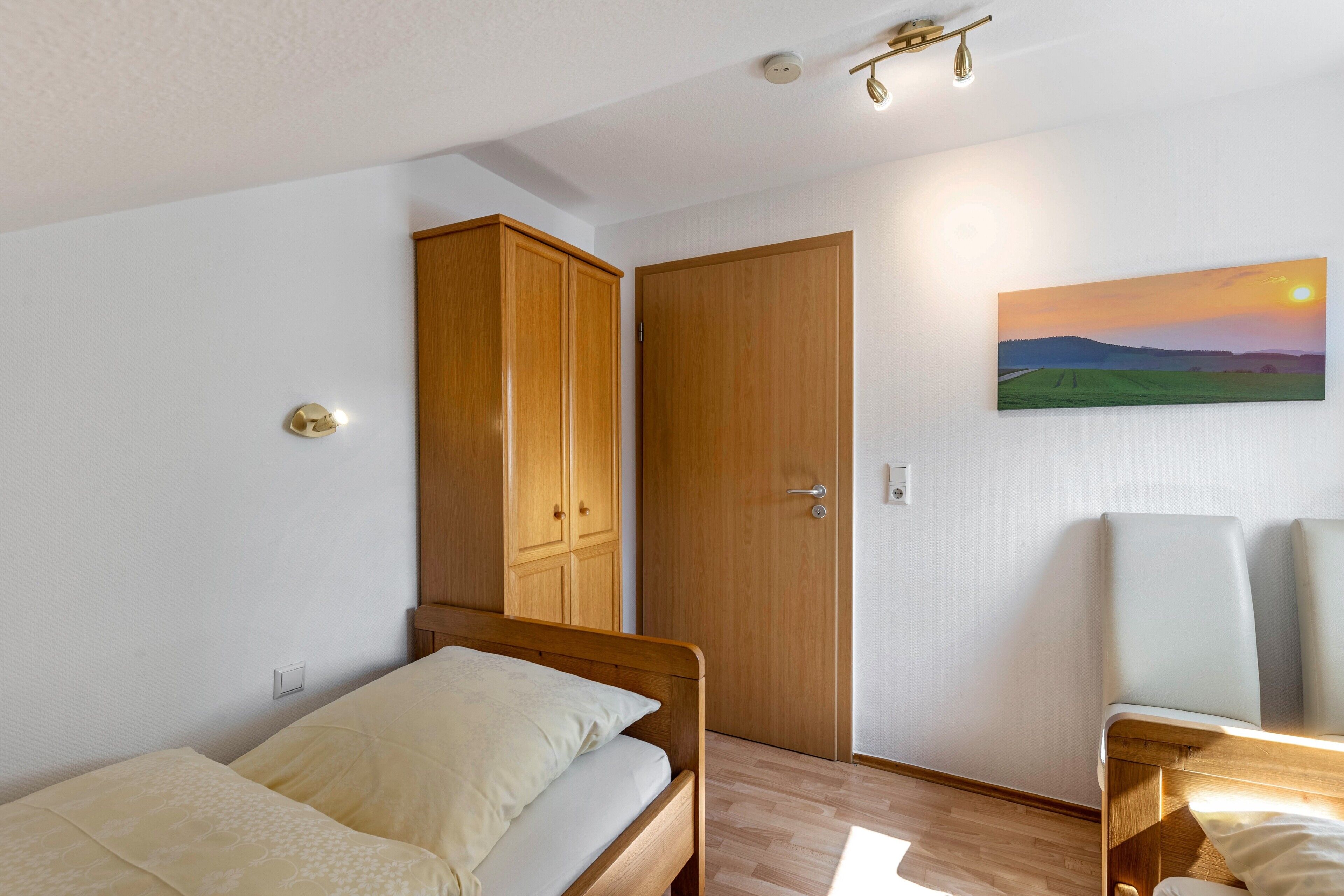 A bedroom with a bed, a wardrobe, a door, and a painting on the wall.