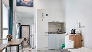 Camera d'albergo compatta con angolo cottura, un letto, un tavolino con una pianta in vaso e vista mare.