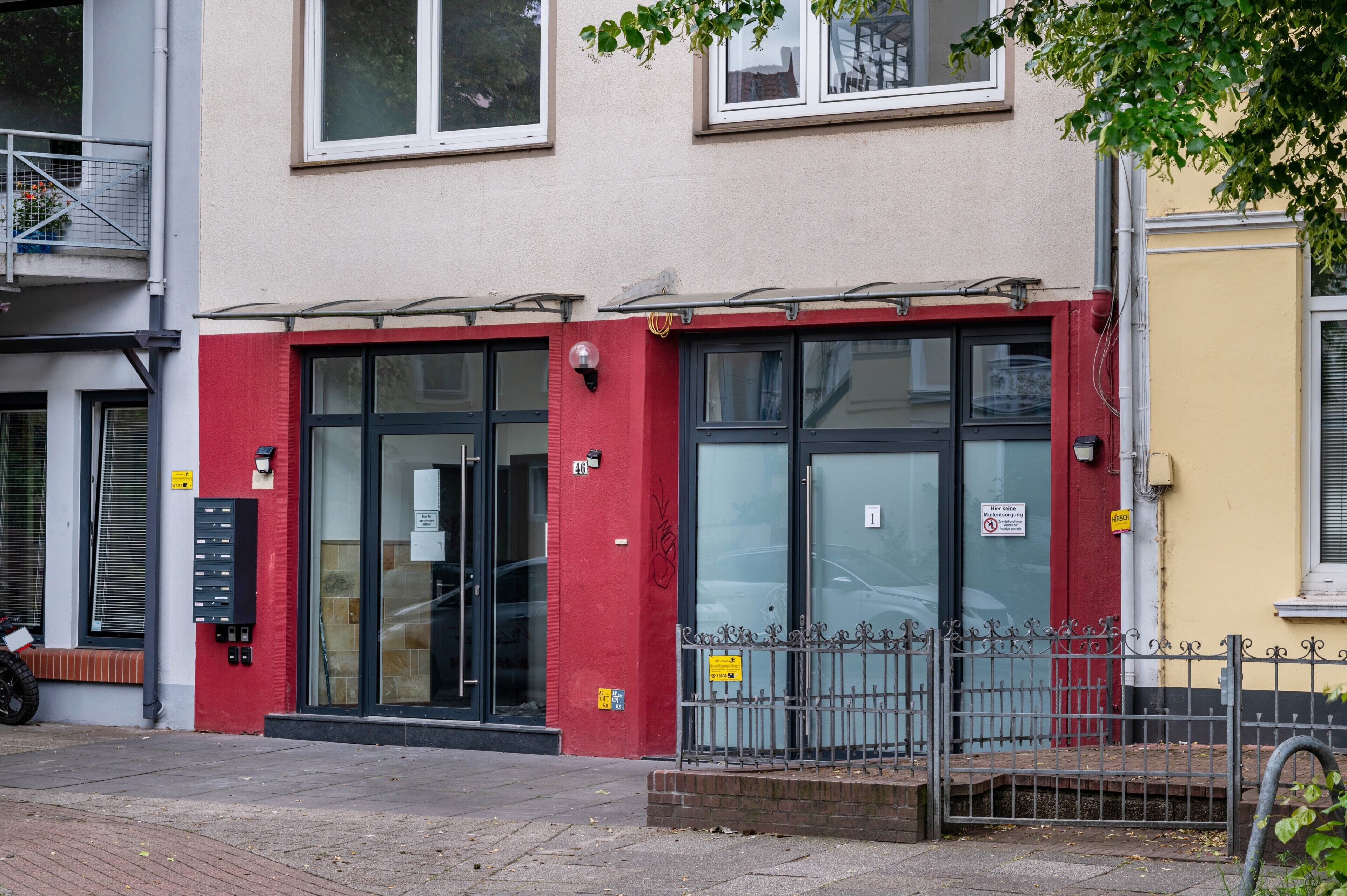 A building with a red facade, large glass doors, and a metal fence in front.
