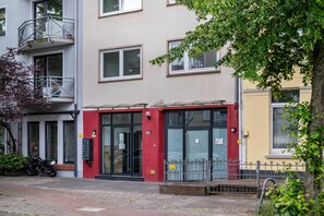Un bâtiment avec une porte rouge, un balcon doté d’une rambarde en métal et un arbre au premier plan.