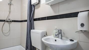 Un bagno con doccia, WC, lavandino e dispenser per sapone.