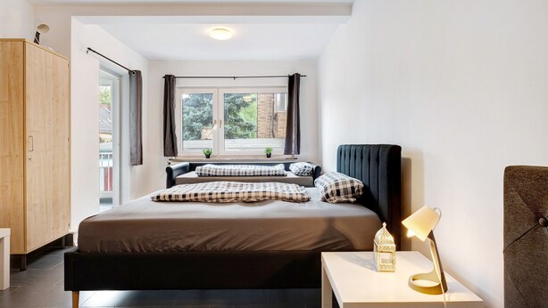 A bedroom with a bed, bedside table, lamp, and window.