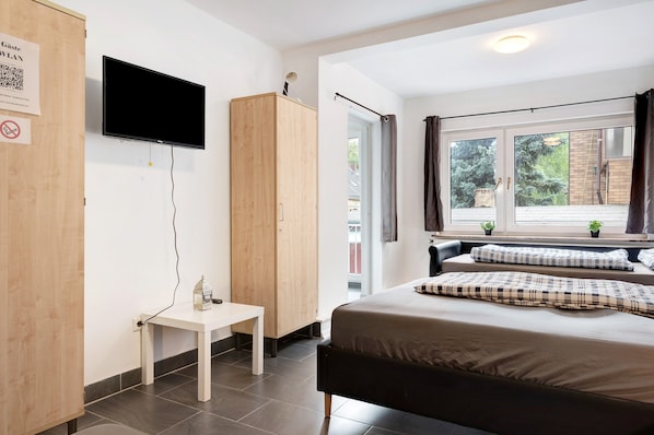 A bedroom with a bed, a TV, a wooden wardrobe, a small table, and a window with curtains.