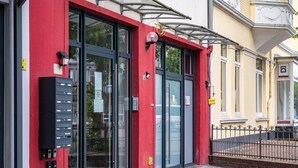 A building with a red facade, large glass doors, a black mailbox, and a metal fence.
