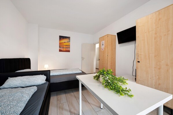 A modern room with a bed, a small sofa, a table with a plant, and a TV mounted on the wall.