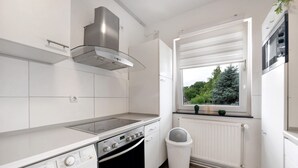Uma cozinha compacta com forno embutido, exaustor de aço inoxidável, janela com vista para o verde e radiador branco.