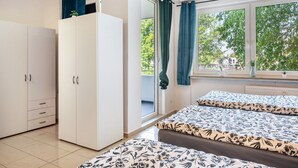 Un dormitorio con cama, armario, ventana con cortinas y vistas a árboles.