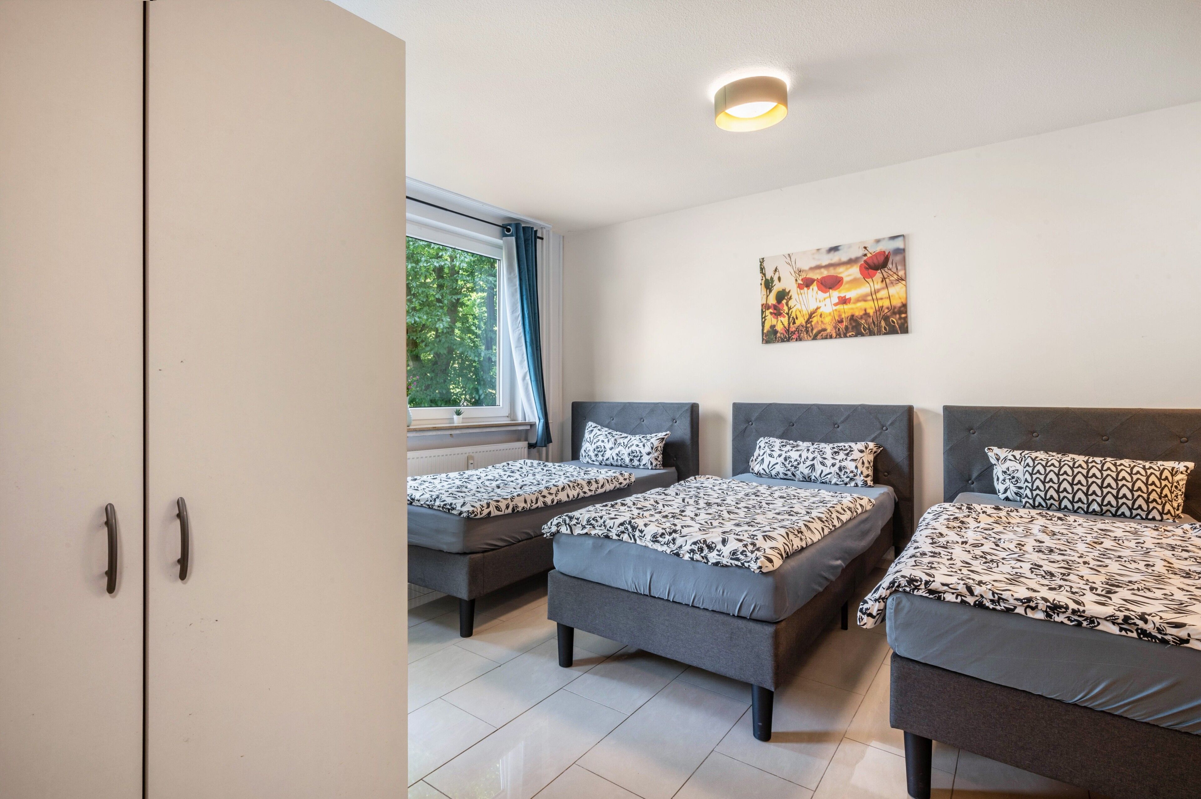 Una habitación con tres camas, una ventana con cortinas, un cuadro en la pared y un armario.