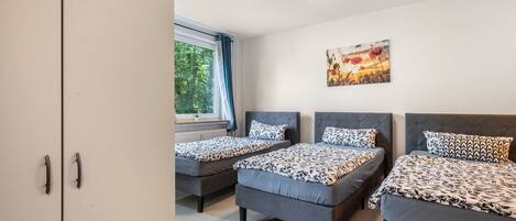Una habitación con tres camas, una ventana con cortinas, un cuadro en la pared y un armario.