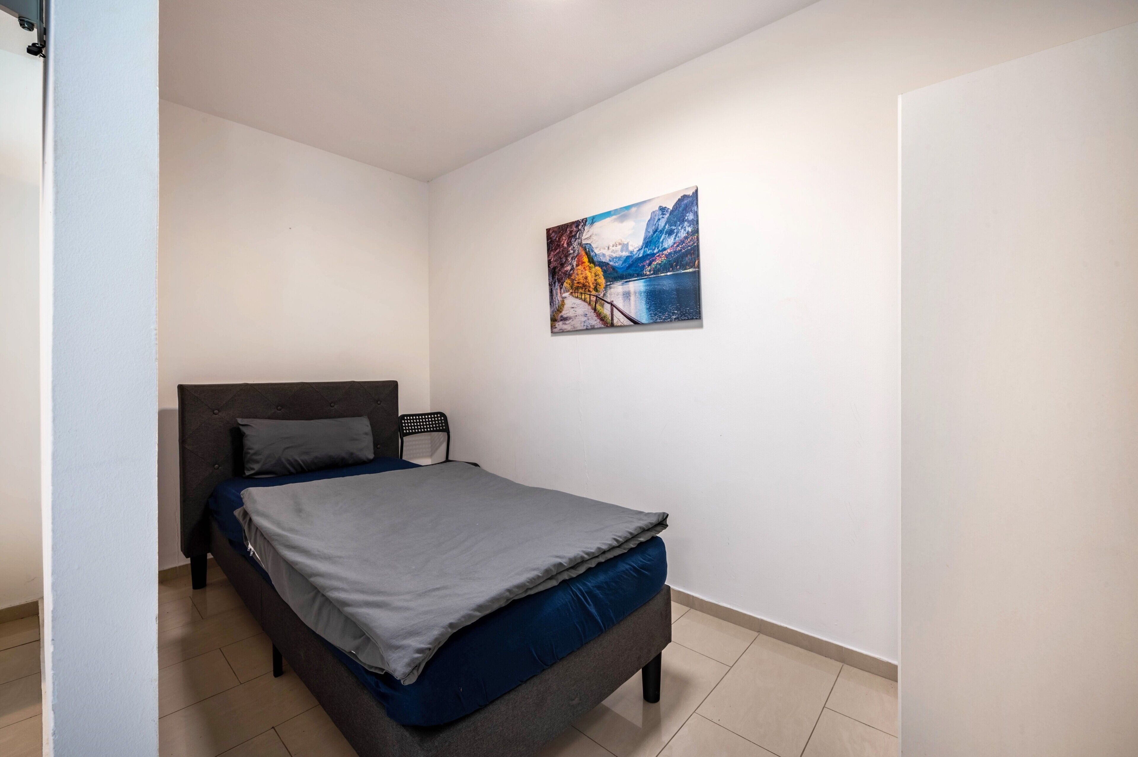 Quarto com cama, mesa de cabeceira, quadro na parede e porta.