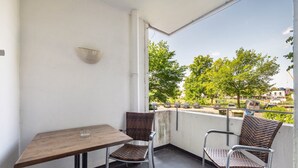 Un balcón con una mesa y dos sillas de mimbre, con vistas a un estacionamiento y árboles.