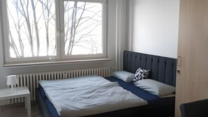 Une chambre à coucher comprenant un lit, un bureau, une chaise, une armoire et une fenêtre donnant sur des arbres sans feuilles.