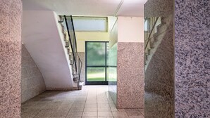 Un pasillo con una escalera, una puerta con una pantalla verde y suelo de baldosas.