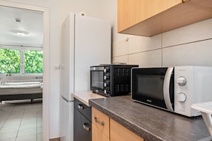 A kitchen with a refrigerator, two microwaves, a toaster, and a bench.
