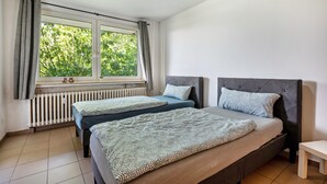 Un dormitorio con dos camas, una ventana con cortinas, un radiador y una mesita.