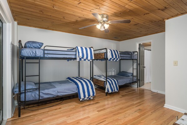 A room with three bunk beds, wooden flooring, a ceiling fan, and a door. - 3-bdrm cabin in Ellijay, gated community, outdoor firepit and pool access (Ellijay)