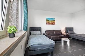 A modern bedroom with a bed, a sofa, a small table, a potted plant, and a painting on the wall.