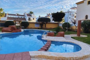 A swimming pool with a stone deck, surrounded by greenery and residential buildings.