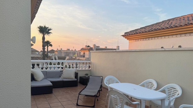 A terrace with a sofa, lounge chairs, and a table.