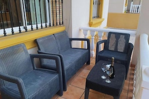 A balcony with wicker furniture, a bottle of champagne, and glasses.