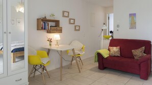 A compact living space with a bed, a dining table with chairs, a red sofa, and a small kitchen area.