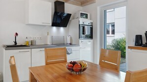 Uma cozinha moderna com armários brancos, uma mesa de jantar de madeira e uma fruteira.