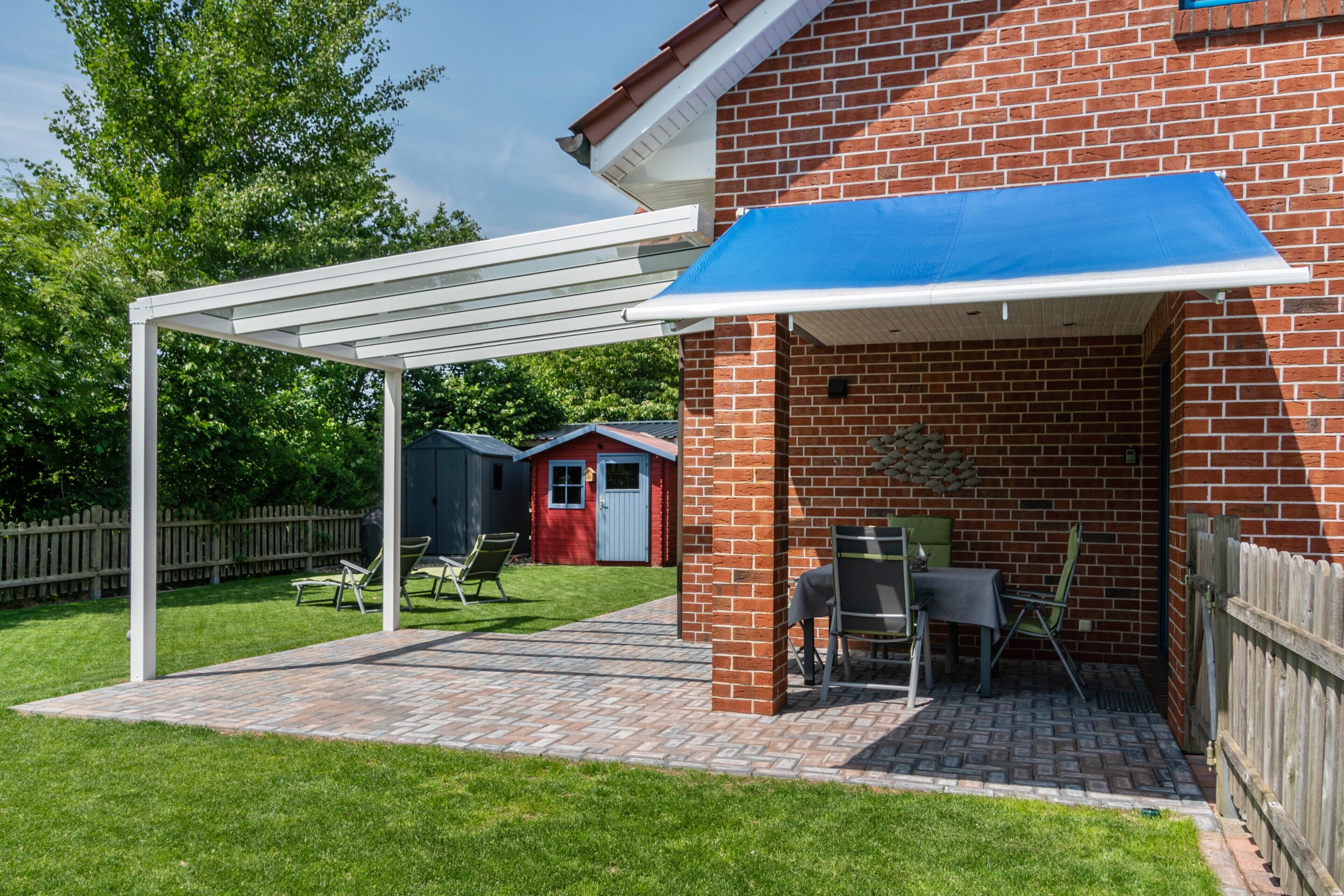 En overdækket terrasse med en murstensvæg, en hvid pergola og et bord med stole.