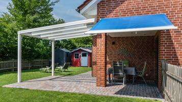 En overdækket terrasse med en murstensvæg, en hvid pergola og et bord med stole.