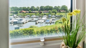 A view of a marina with boats docked, greenery, and houses in the background. - Holiday Home 'Hafenblick' with Private Terrace, Private Garden and Wi-Fi (Walchum)