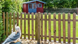 A wooden fence, a bird sculpture, and a red building in the background. - Holiday Home 'Hafenblick' with Private Terrace, Private Garden and Wi-Fi (Walchum)