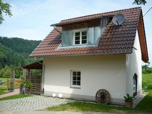 Una casa a un piano con tetto spiovente, un’antenna parabolica, un piccolo oblò e una carriola.