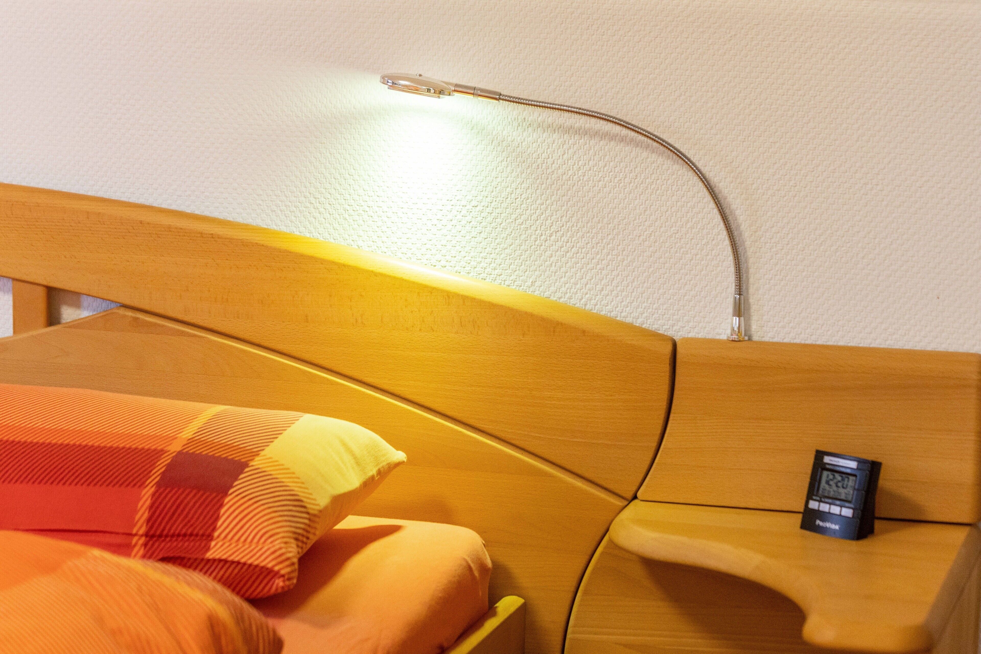 A bed with a wooden headboard, a bedside table with a clock, and a pillow with a checkered pattern.