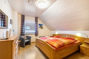 A bedroom with a wooden bed, a desk, a chair, a window with curtains, and a ceiling light.