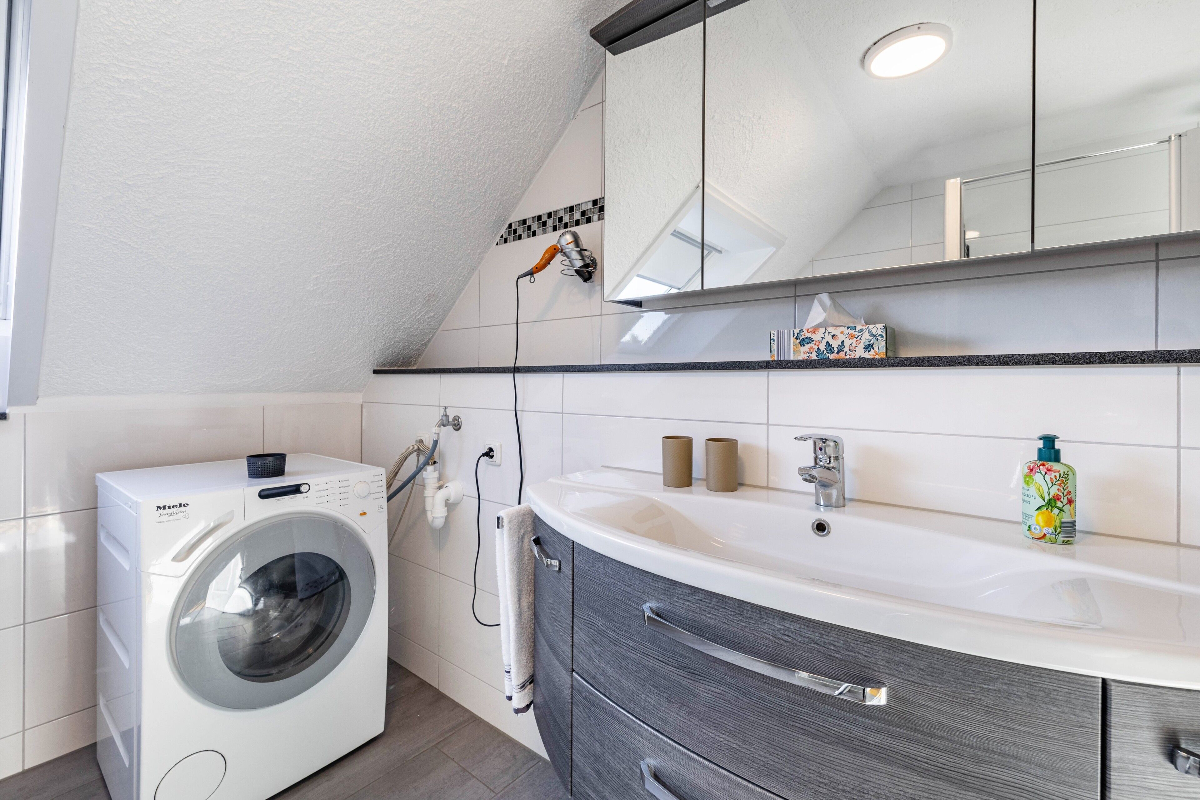 Ein modernes Badezimmer mit Waschmaschine, Waschbecken und Spiegel.