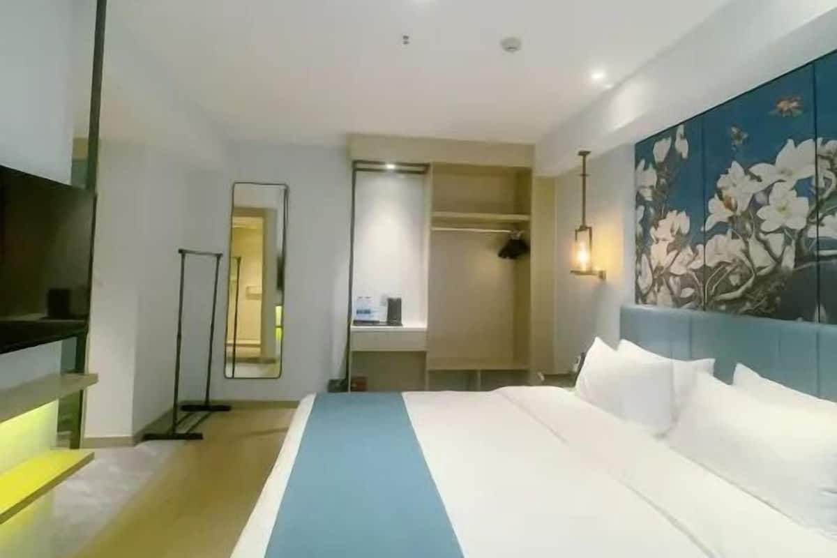 A modern hotel room with a large bed, a wardrobe, a mirror, and a painting on the wall.