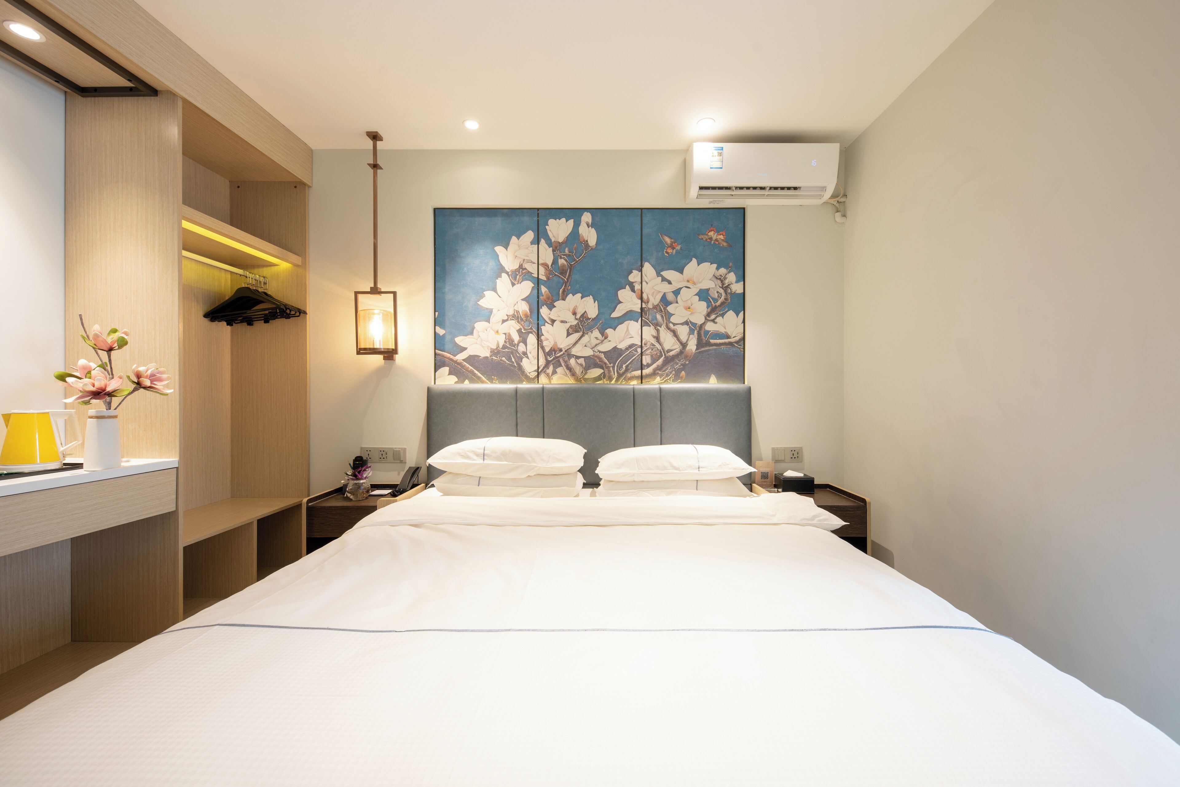 Una habitación de hotel con cama, mesitas de noche, aire acondicionado instalado en la pared y un cuadro de flores.