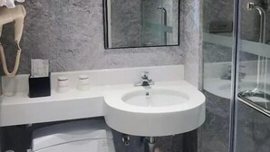 Une salle de bain moderne avec un mur en marbre, un lavabo blanc, une cabine de douche en verre et des toilettes.