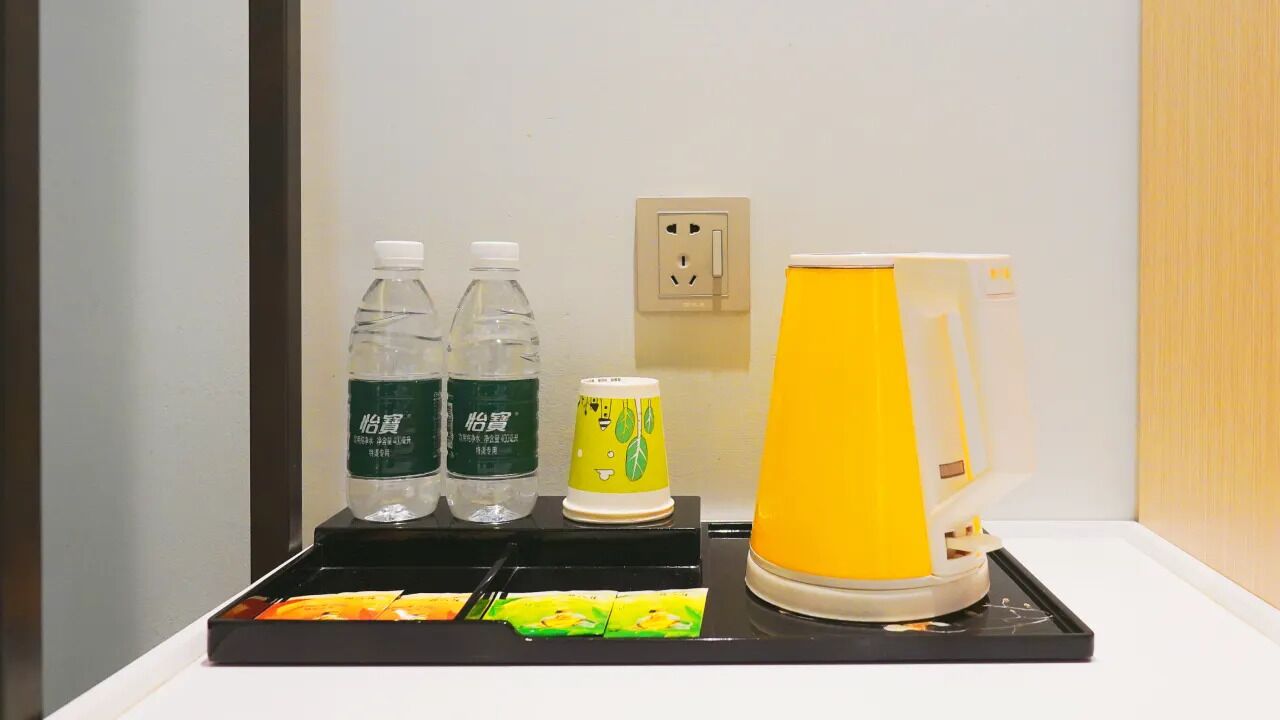 A hotel minibar with bottled water, a can of drink, and a yellow appliance, likely a coffee maker, on a tray.