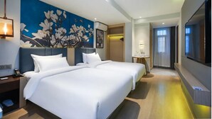 Une chambre d’hôtel avec deux lits, une grande fresque murale à motifs floraux, un téléviseur à écran plat et une petite table avec une lampe.