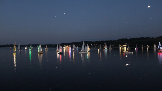 A calm lake at night with sailboats reflecting on the water.