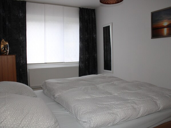 Een slaapkamer met twee bedden, een radiator, een raam met gordijnen en een schilderij aan de muur.