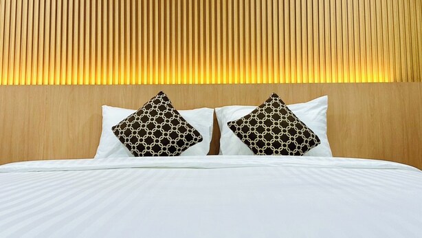 A hotel room with a wooden headboard, white bedding, and two patterned pillows. - The Cozy 77 - No Parking (Bangkok)